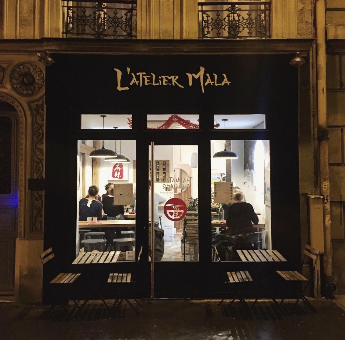 Façade d'Atelier Mala la nuit, salle éclairée et terrasse vide